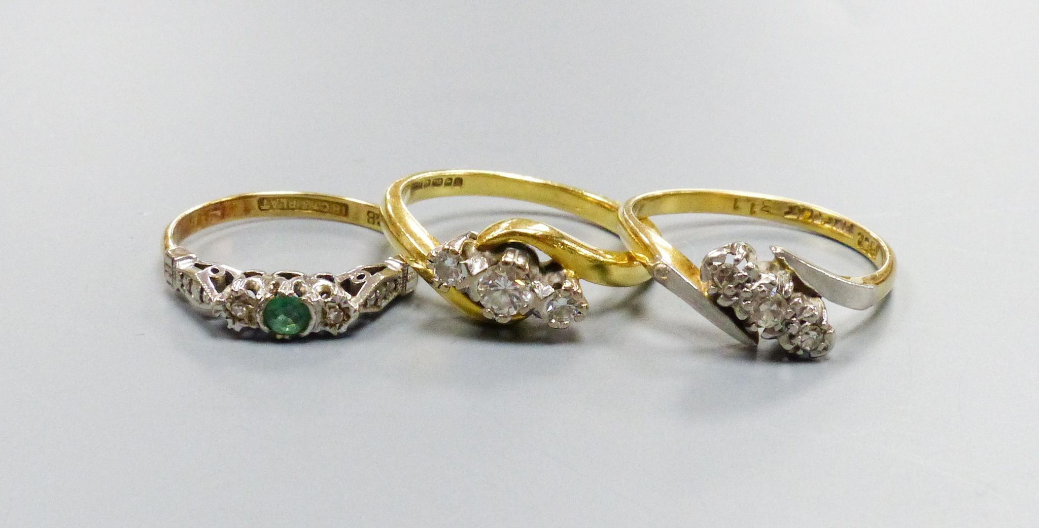 Two 18ct and three stone diamond set crossover rings, sizes K and N and an 18ct & plat, emerald and diamond set three stone ring, size J, gross weight 8.2 grams.